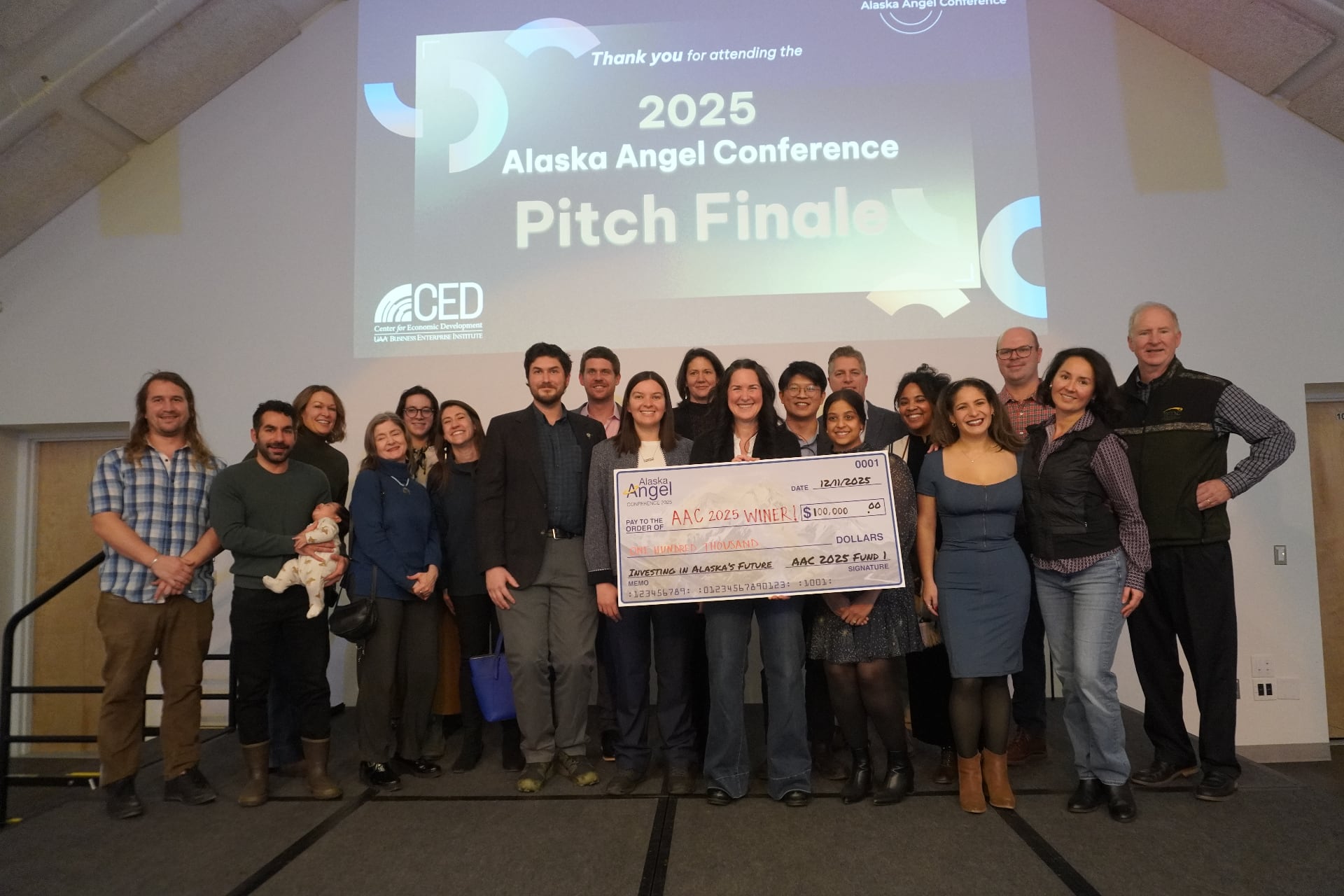 The 2025 Alaska Angel Conference cohort on stage with the winning startup holding a $100,000 check